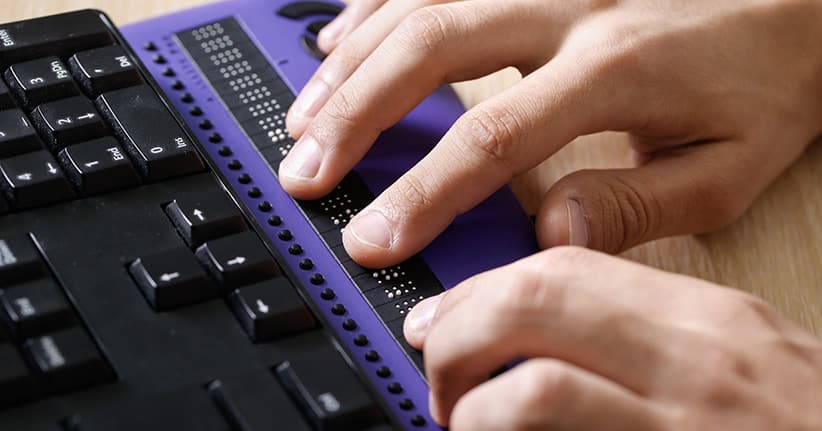 Ein blinder Mensch benutzt eine Standard-Windows-Tastatur mit integrierter Braille-Schrift.