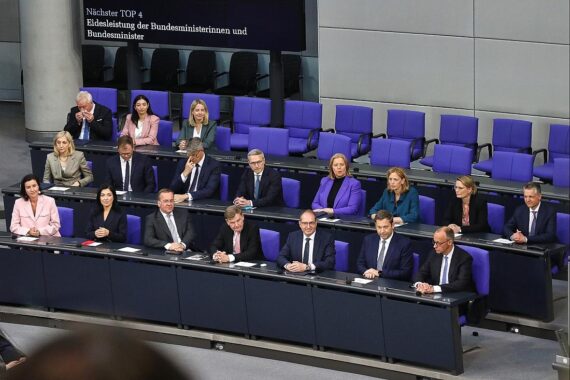 Das neue Kabinett Merz auf der Regierungsbank, symbolisiert politische Veränderungen und zusätzliche Stellen.