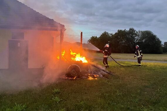Feuerwehrfahrzeuge löschen brennenden Anhänger neben Gebäude in Mülheim an der Ruhr.