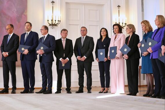 Bundesregierungssitz mit vielen Menschen, Zeichen der Kritik an Personalaufbau, finanzielle Belastung für Steuerzahler.