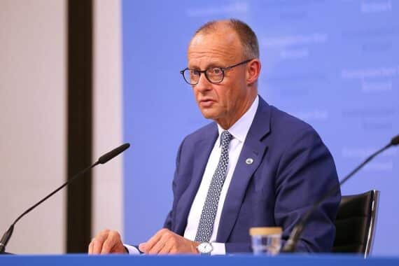 Friedrich Merz spricht vor Publikum, umgeben von politischen Symbolen der CDU und CSU.