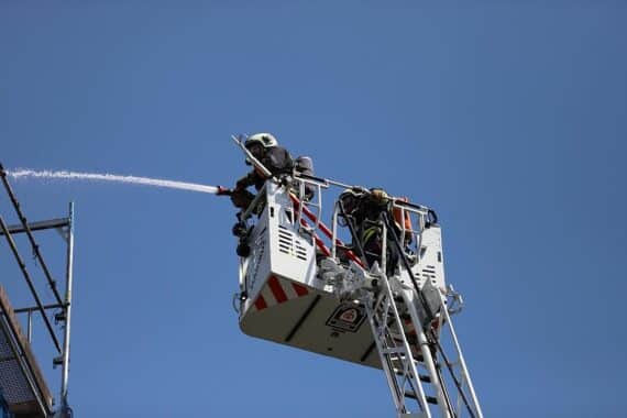 Feuerwehrlöscheinsatz bei Scheunenbrand; zerstörte Gebäude und landwirtschaftliche Maschinen sichtbar.