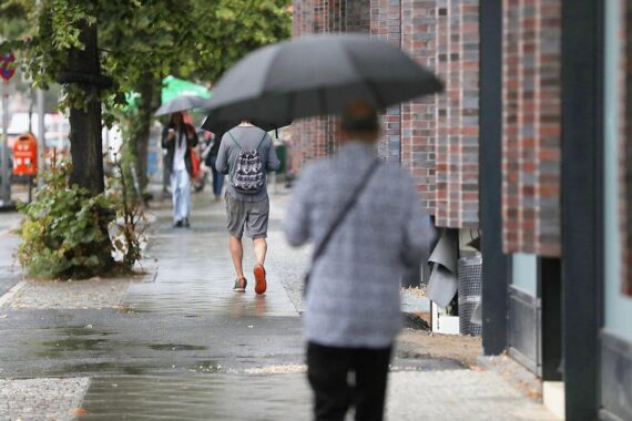 Passanten mit Regenschirmen bei Regen in Schleswig-Holstein, symbolisieren die unbeständige Juni-Wetterlage.