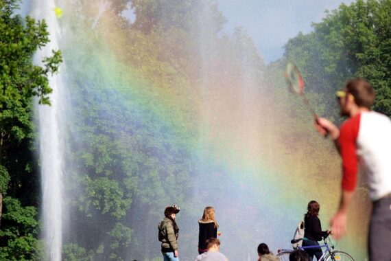 Sonniger Park mit Grünflächen, blühenden Pflanzen und Menschen, bevor Gewitter aufziehen.