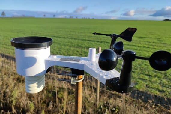 Wetterstation im Ackerbereich, mit wechselnd bewöltem Himmel und Wassertropfen auf Pflanzen.