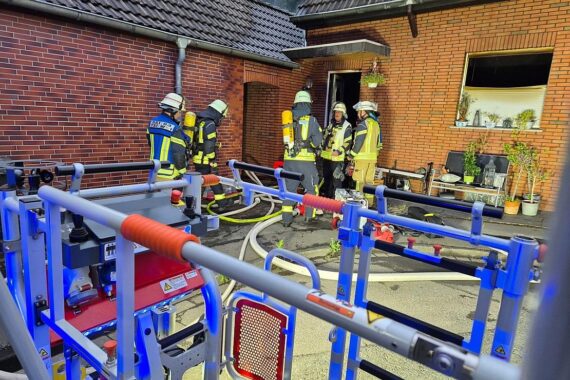Feuerwehr im Einsatz bei Wohnungsbrand, Flammen und Rauch aus Erdgeschoss eines Reiheneckhauses.