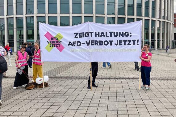 Protestierende Menschen gegen AfD-Verbot, Plakate, demokratische Auseinandersetzung, symbolische Darstellung von Meinungsfreiheit.