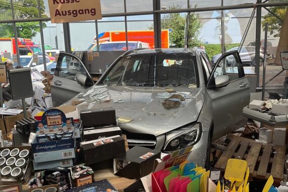 Ein Mercedes durchbricht Schaufenster; Unfallort mit Fahrzeug und beschädigtem Laden zu sehen.