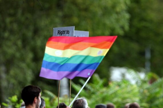 Regenbogen-Fahne schwingend, Demonstranten marchieren für queere Rechte durch Bonn. Sicherheitskräfte begleiten.