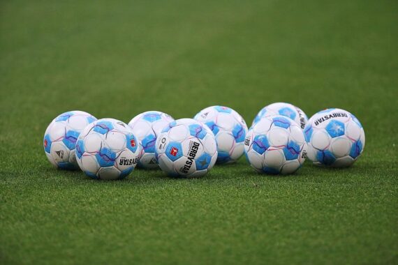 Ein Fußballfeld mit Dynamo-Dresden- und FC-Energie-Cottbus-Logos, symbolisiert den Spielerwechsel.