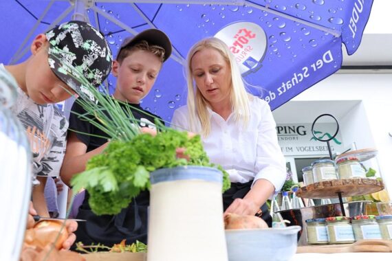 Familienministerin Diana Stolz pflanzt mit Kindern Kräuter im Garten des Kolping-Feriendorfs.