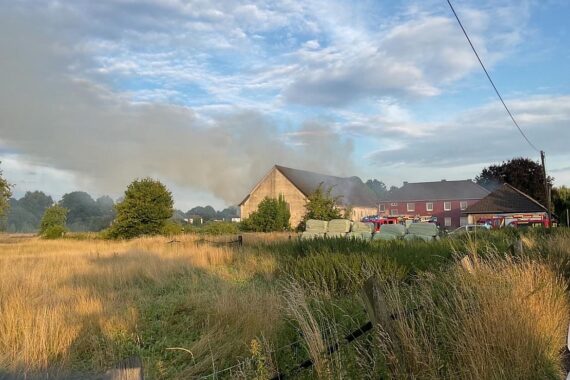Einsatzfahrzeuge der Feuerwehr vor brennender Scheune, Einsatzkräfte und Rauchentwicklung sichtbar.