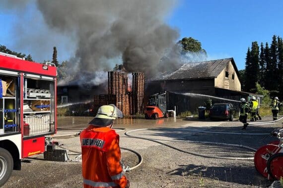 Löscharbeiten durch Feuerwehr bei großem Brand in Lagerhalle, starke Rauchentwicklung sichtbar.