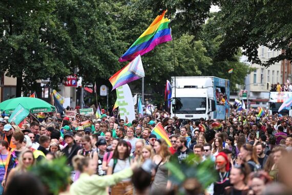 Bunte Parade mit fröhlichen Menschen, Regenbogenflaggen und Polizeipräsenz in Berlin während CSD.