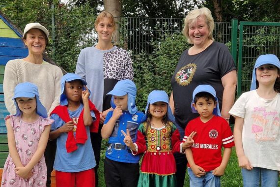Kinder mit Sonnenschutzmützen spielen im Freien, betreut von Erzieherinnen in der Kita.