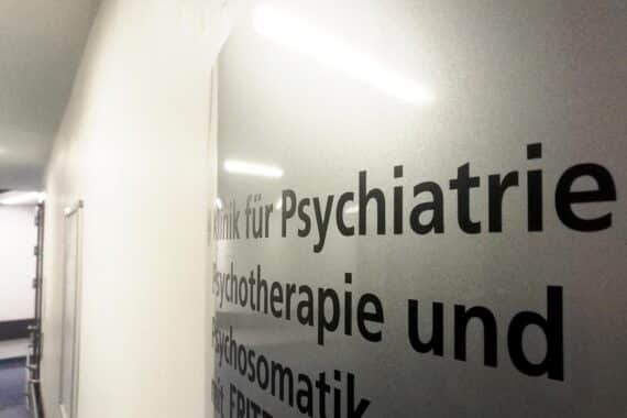 Wartezimmer einer Psychiatrie mit überfüllten Sitzen und ungeduldigen Patienten.