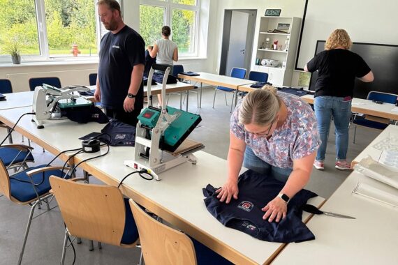 Zwei Feuerwehrleute in neuen einheitlichen Shirts mit Wappen, symbolisieren Gemeinschaft und Zusammenhalt.