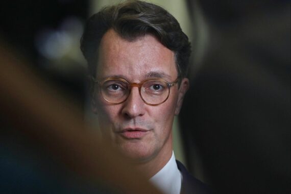 Ein Porträt von Hendrik Wüst, Ministerpräsident NRW, vor einem Hintergrund politischer Diskussionen.