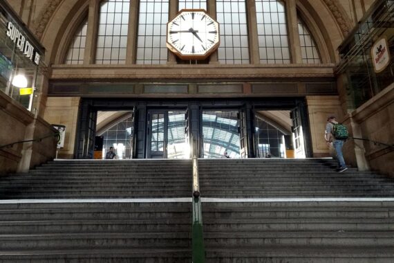 Bahnhofsuhr im Leipziger Hauptbahnhof mit Szene des Polizeieinsatzes und einem verwirrten Mann.