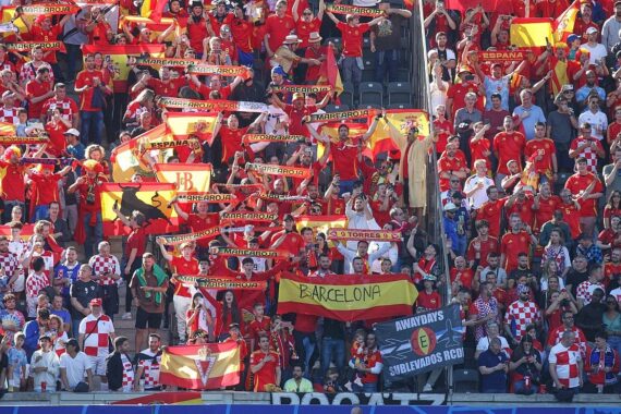 Eine jubelnde Gruppe spanischer Fußballfans mit Trikots und Fahnen im Stadion.
