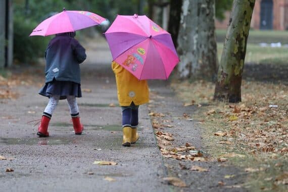 Zwei Kleinkinder im Freien, orange-blättrige Bäume, wechselhaftes Wetter mit Wolken und Sonne.