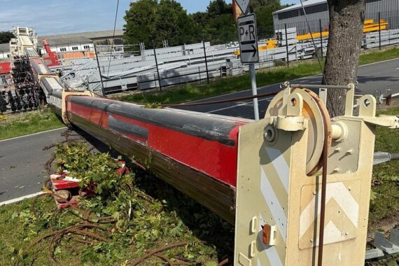 Umgekippter Kran mit ausgefahrenen Teleskoparmen auf Firmengelände, Rad-/Gehweg und B 195 blockiert.