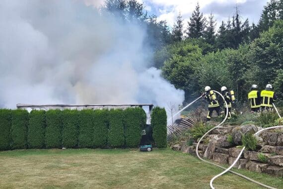 Feuerwehr im Einsatz, brennende Hobbywerkstatt, gesperrte Straße, Gefahr durch Gasflaschen.