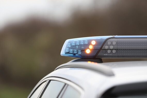 Polizeiauto an Unfallstelle mit beschädigten Fahrzeugen und Umleitungshinweisen, Verkehrsteilnehmer beobachten.