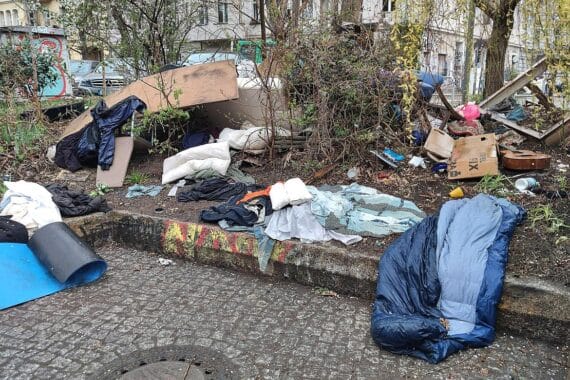 Ein Obdachlosen-Camp unter einer Brücke, umgeben von Müll und Protesten für Unterstützung.