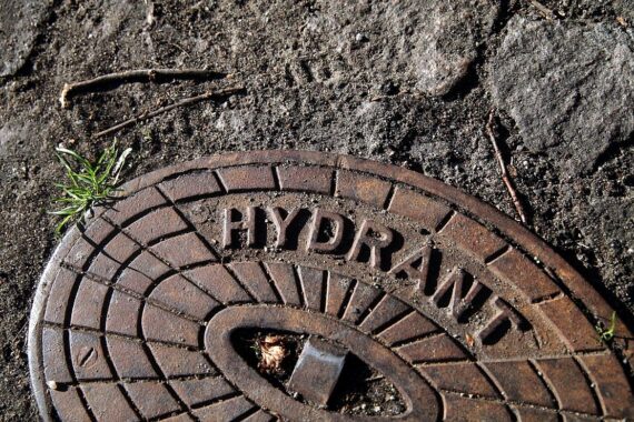 Ein beschädigter Wasserhydrant, umgeben von Wasserfontänen, Zeugen beobachten das Geschehen.