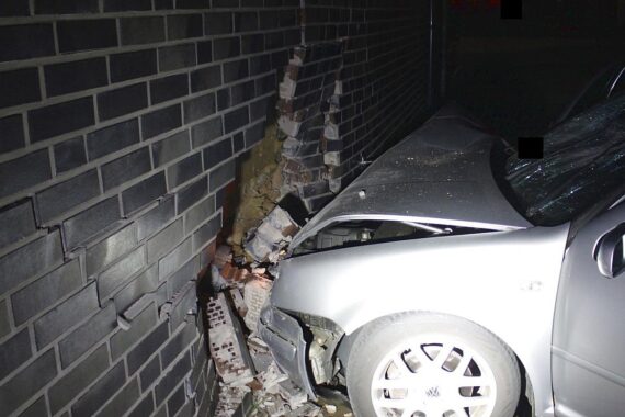 VW Golf kollidiert mit Hauswand nach riskantem Überholen; Polizei sucht flüchtige Audi-Insassen.