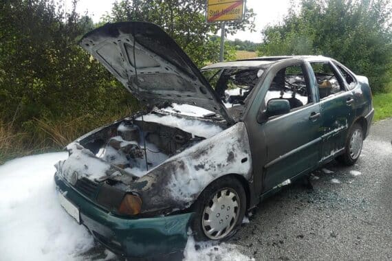 Ein Feuerwehrmann löscht einen brennenden VW Polo an der Straße in Arendsee.