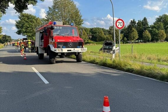 Ein Unfallfahrzeug in der Wiese, Feuerwehr, Rettungsdienst und abtransportierte Verletzte im Hintergrund.