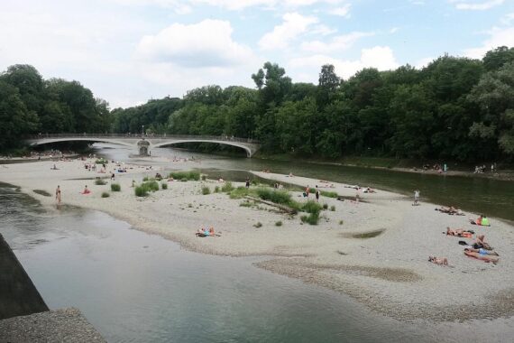 Sonniger Isarstrand in München, Menschen genießen den Sommer, strahlend blauer Himmel.