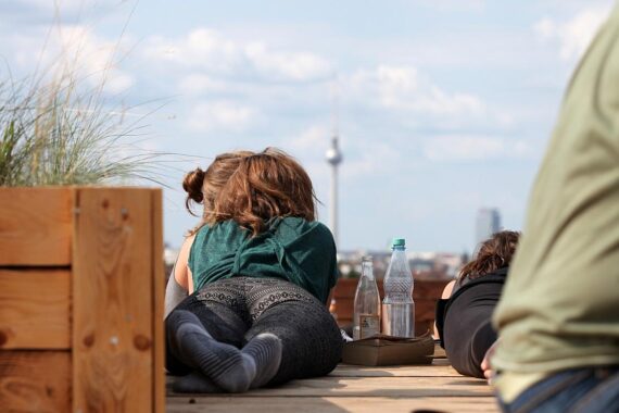 Junge Frau genießt Sommerabend mit Getränken und Blick auf Berliner Fernsehturm von Dachterrasse.