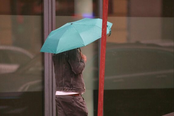 Mann mit Regenschirm in wechselhaftem Wetter, zeigt Regen und mögliche Gewitter.