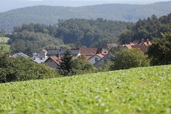 Dorfhaus mit Garten, in dem Zeckenwarnung und Schutzmaßnahmen vor FSME sichtbar sind.