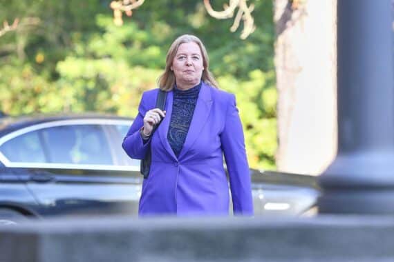 Bärbel Bas lächelt optimistisch, blickt in die Kamera, im Hintergrund politische Diskussionen.