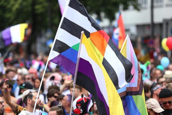 Bunte Parade mit Menschenmengen, fröhlichen Flaggen und Polizeipräsenz während Christopher Street Day.
