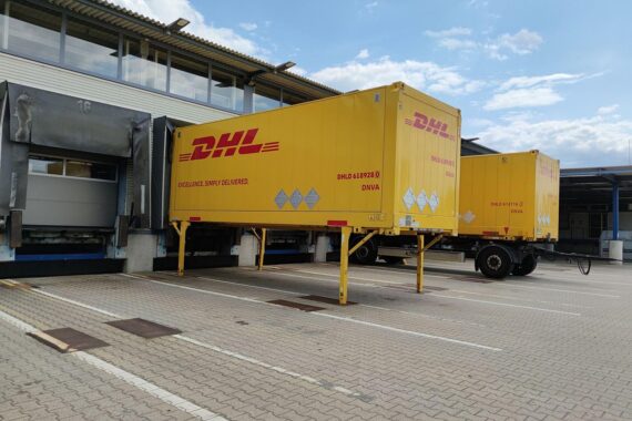 DHL-Logistikzentrum mit Paketen und Mitarbeitenden, Symbol für wirtschaftliche Herausforderungen und politische Stabilität.