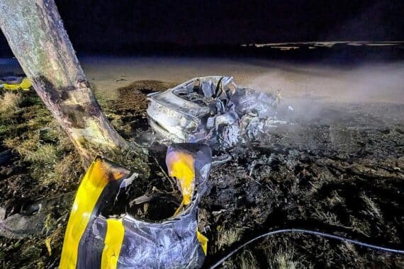 Schockierende Unfallstelle mit einem brennenden Auto und Einsatzkräften der Feuerwehr und Rettung.