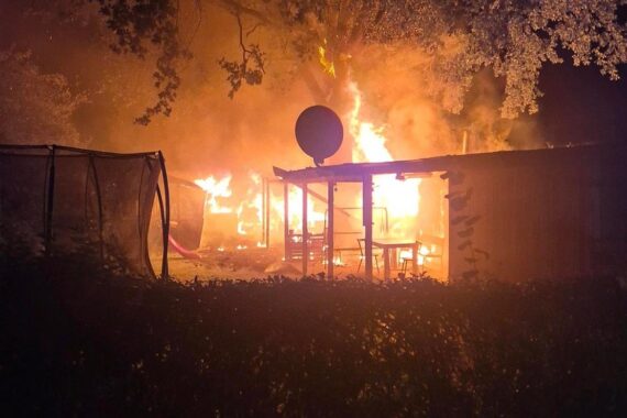 Großbrand in Kleingarten: Feuerwehr bekämpft Flammen, mehrere Schuppen betroffen, Ursachenklärung läuft.