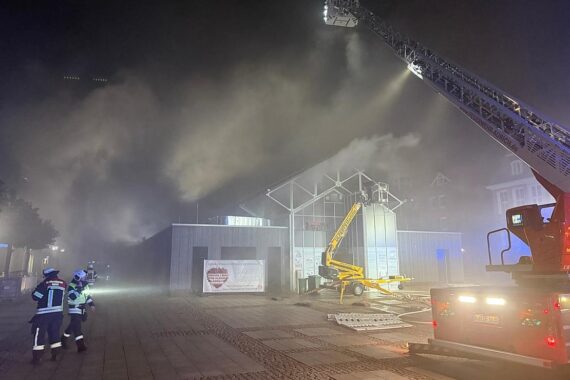 Feuerwehrkämpfer löschen ein Großfeuer in einer Gastronomie-Küche, dichter Rauch über Marktplatz.