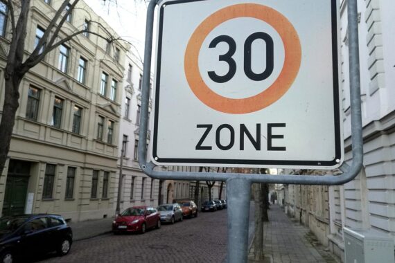 Stadtstraße mit Tempo-30-Schild, Kinder und Fußgänger, Sicherheit und Verkehrspolitik im Fokus.