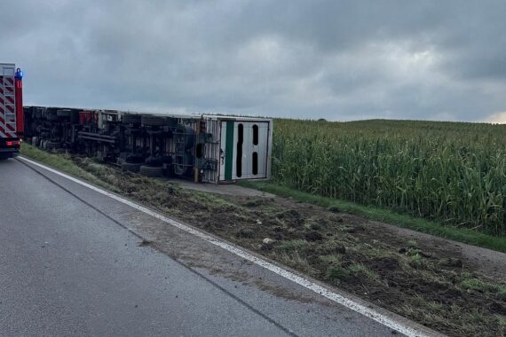 Verunglückter Sattelzug auf Feldweg, Polizei und Bergungsarbeiten im Hintergrund sichtbar.