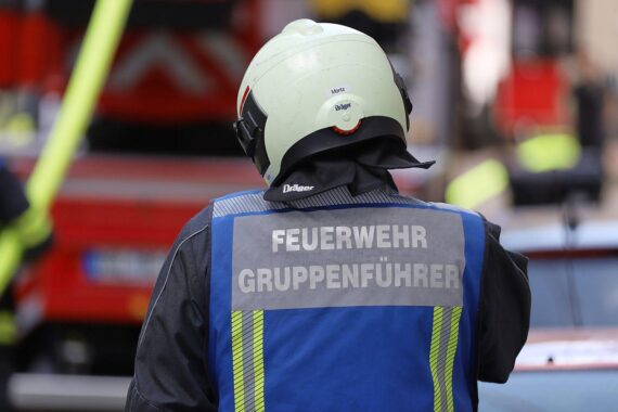 Feuerwehrleute helfen verletztem Mann nach Straßenbahnunfall in München, Einsatzort unscharf im Hintergrund.
