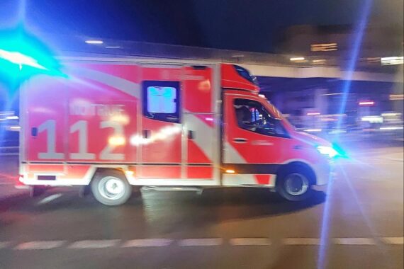 Rettungswagen vor Unfallstelle, beschädigte Fahrzeuge, Polizei vor Ort, regennasse Autobahn.