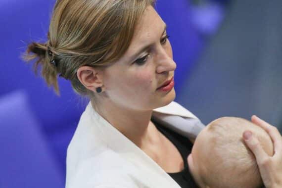 Politikerin mit Baby in Trage, symbolisiert Vereinbarkeit von Familie und politischem Engagement.