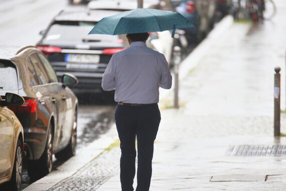 Mann mit Regenschirm in nebliger, wechselhafter Wetterlage, symbolisiert lokale Schauer und Gewitter.