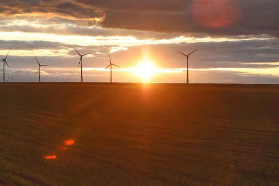 Windräder vor wechselhaftem Himmel, symbolisieren Wetterumschwung mit Sonne, Wolken, Regen und Gewitter.